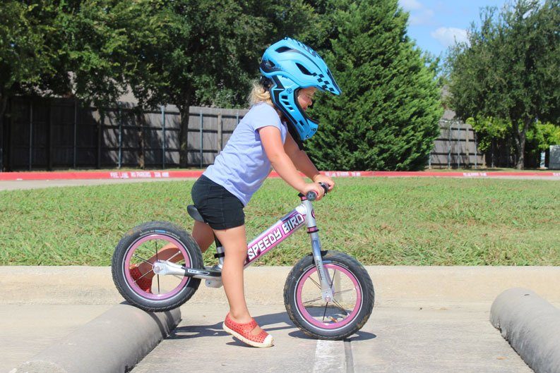 Toddler riding her Strider bike over a curb while wearing the Strider Full Face helmet