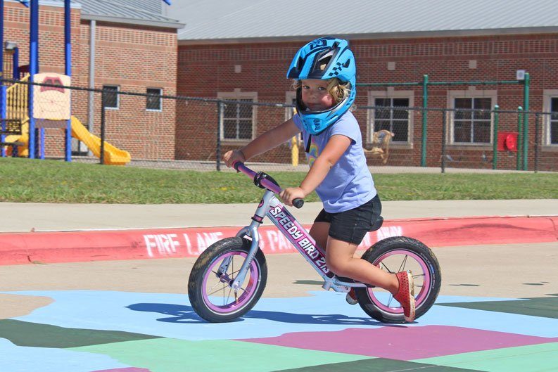 2 year old toddler riding her Strider bike and wearing a Strider Full Face helmet