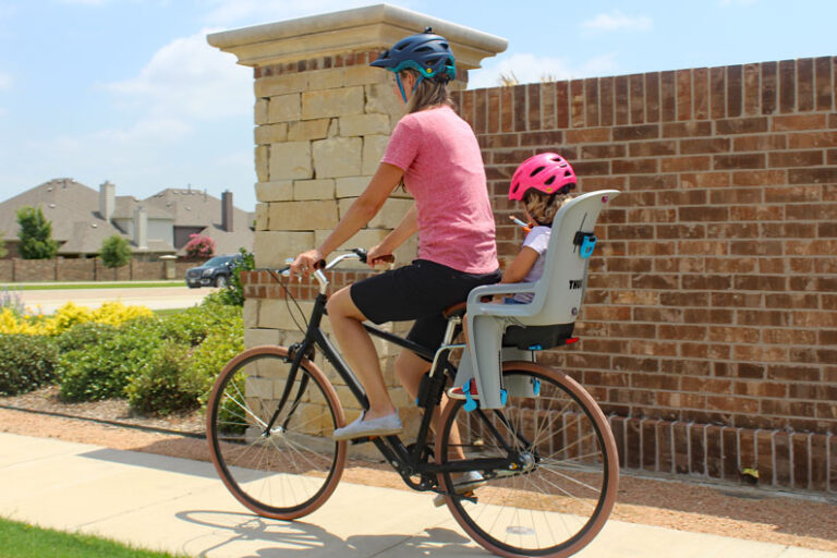 Mom riding Priority bicycle with toddler on the back in Thule RideAlong child bike seat from the rear.