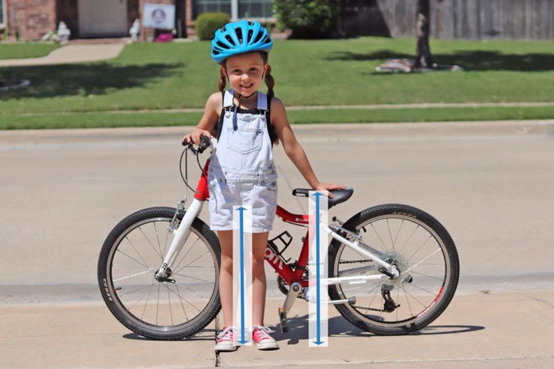 5 year old standing next to her bike. Arrows indicating inseam measurement and bike seat height measurement