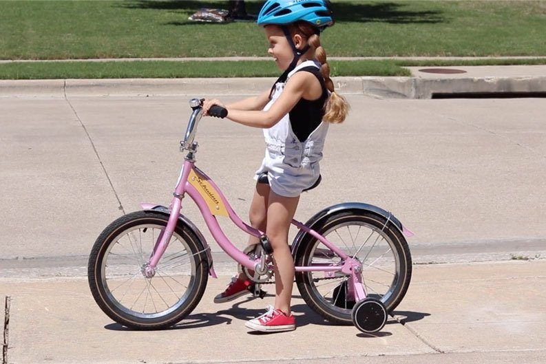 5 year old rider sitting on her bike with training wheels. Feet touching the ground on her tip toes