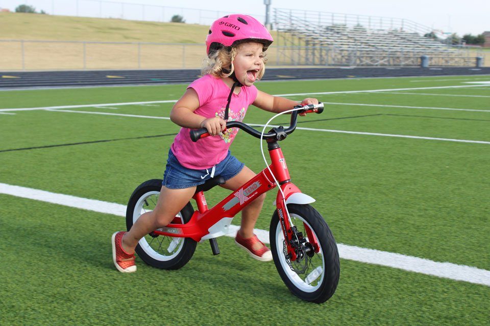 2.5 year old riding Smart Trike XTend Mg Convertible balance bike in balance bike mode across football field.