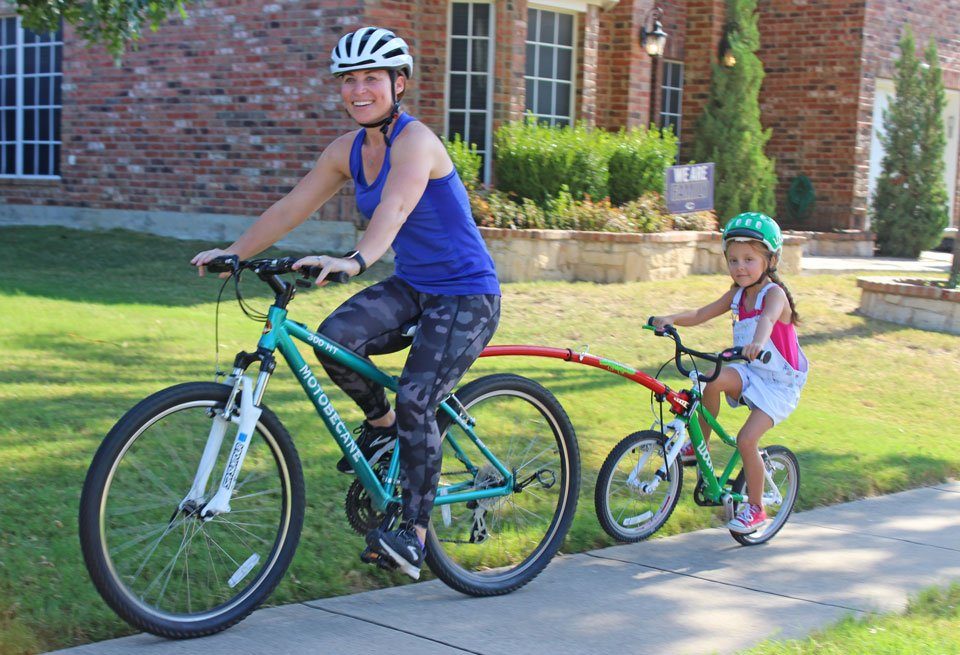 Trail Gator tow bar connected between adult and child bike. Mom and daughter riding together.