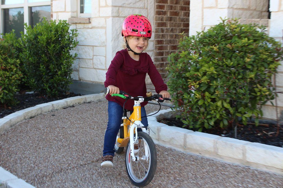 Toddler riding woom 1 plus balance bike and wearing Nutcase Baby Nutty helmet with the Strawberry pattern