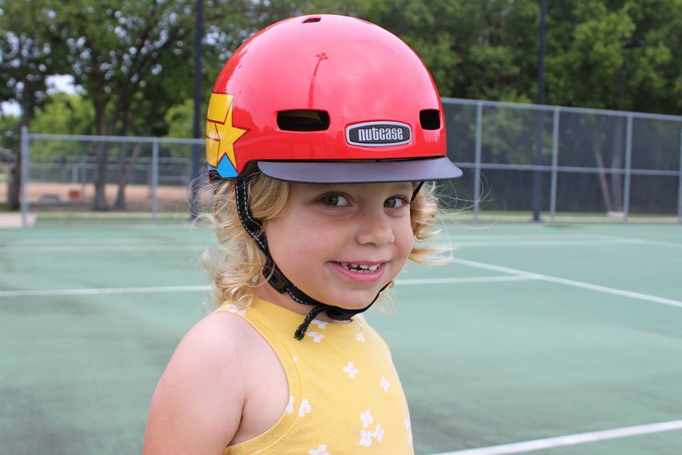 2 year old wearing Nutcase Little Nutty helmet with Wonder Woman pattern. At the tennis court.