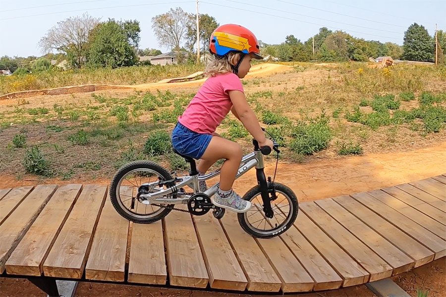Young girl riding a Prevelo Alpha One 14 inch bike on a wooden feature at a bike park