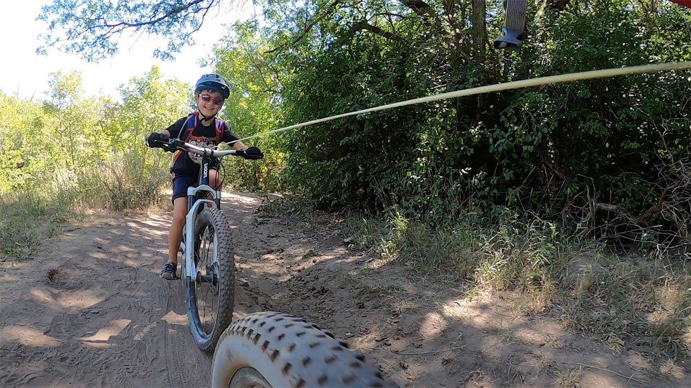 8 year old smiling as he's being pulled up the trail using the TRAXmtb tow rope