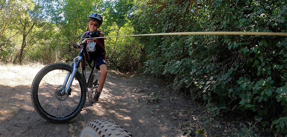 8 year old smiling as he's being pulled up the trail using the TRAXmtb tow rope
