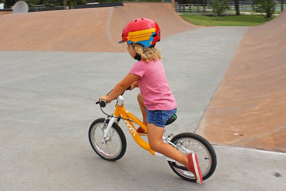 Toddler wearing Nutcase Little Nutty helmet and riding woom 1 plus balance bike at the skate park.