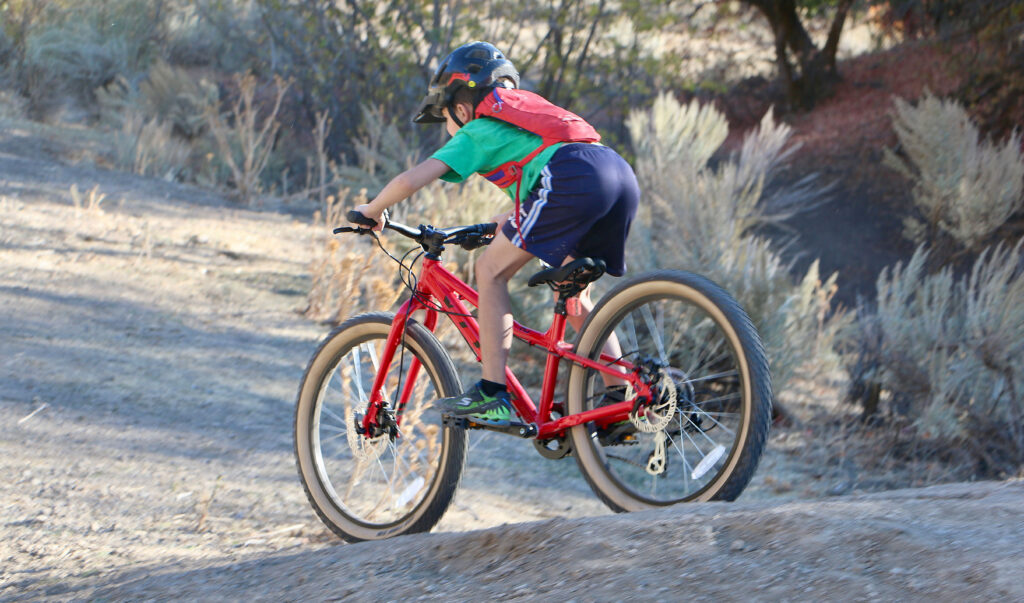 8 year old riding Vitus Plus 24 inch kids bike down a dirt roller, in attack position