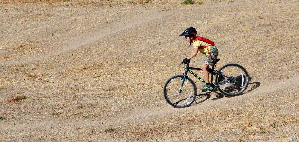 8 year old riding Vitus Kids 24 inch bike down a dirt trail