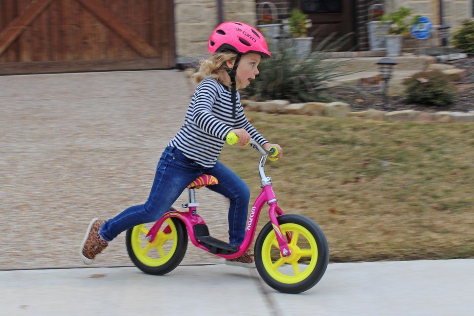 Toddler riding hot pink and yellow Kazam bike down the driveway.