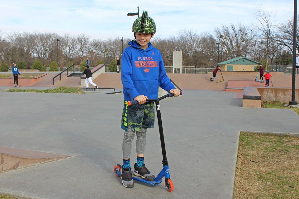 Boy on scooter at the skatepark. Wearing Razkullz Mohawk Dino Helmet