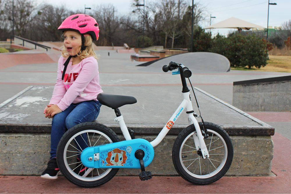 3 year old girl sitting next to her Btwin 14 inch bike at the skatepark