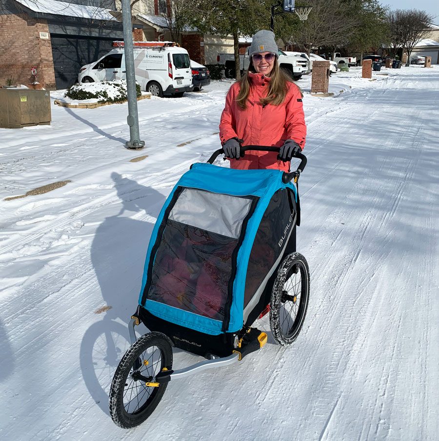 Mom pushing her two kids in a Burley trailer using the Burley Baby Snuggler