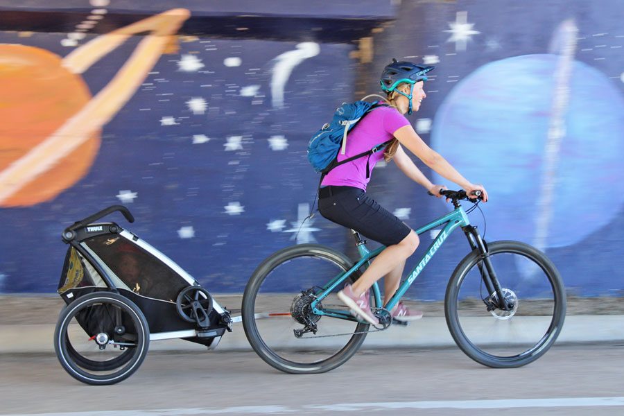 Mom pulling toddler in the Thule Chariot Lite trailer through the street