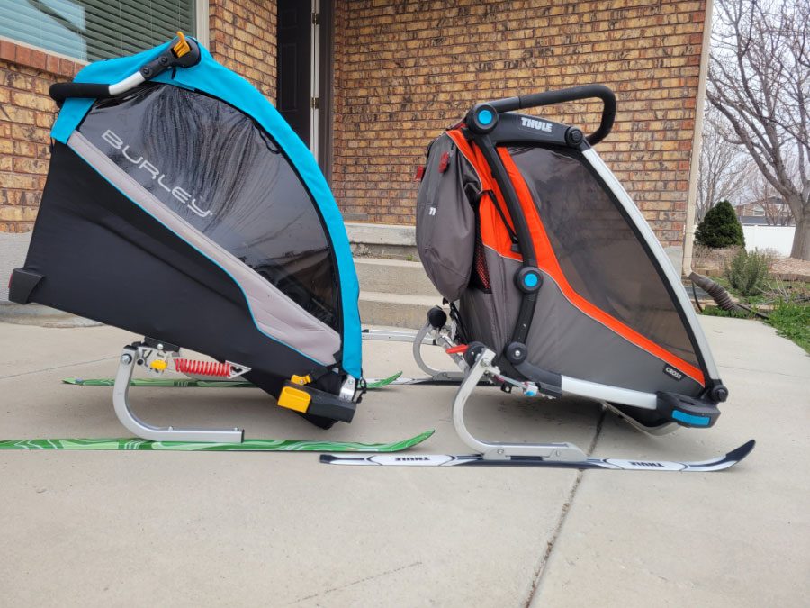 Side by side comparison of Burley D'Lite X and Thule Chariot Cross with the ski kits attached. The Burley leans far forward when in resting position