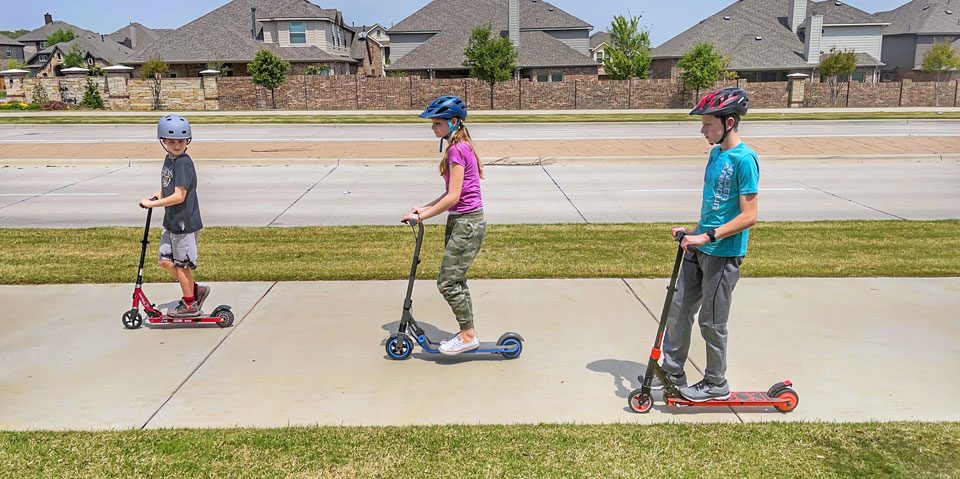 3 kids riding electric scooters down the sidewalk together