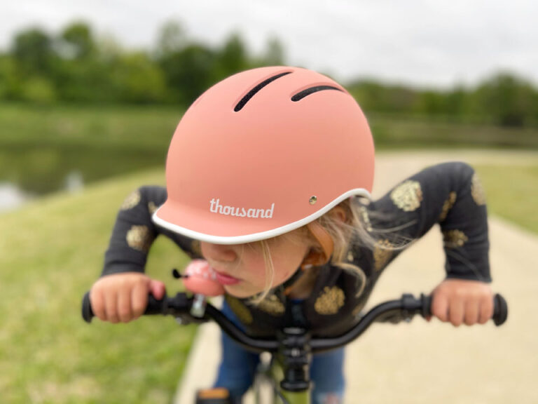 Close up of pink Thousand Jr kids bike helmet while child is leaning forward on bike