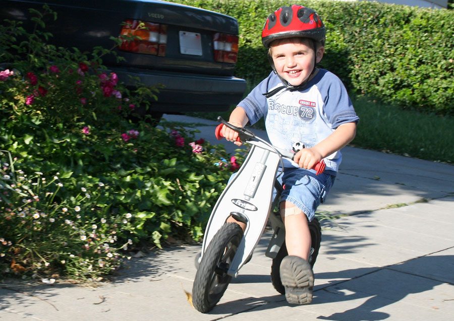 young boy riding the FirstBike Street balance bike on the sidewalk