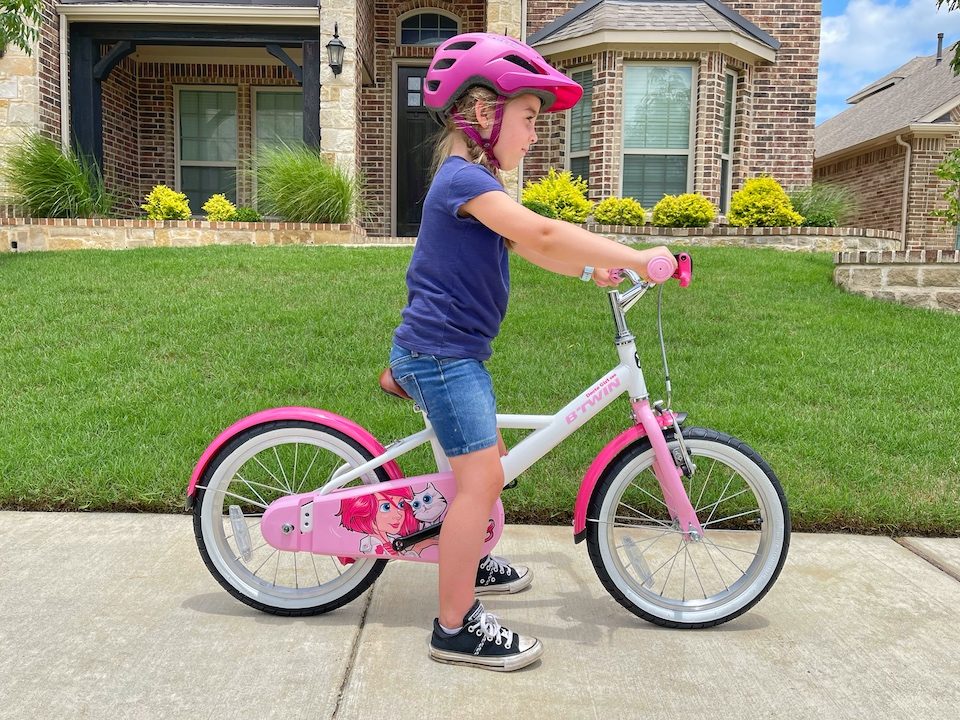 Child sitting on bike with pedals off, slight bend in her knee