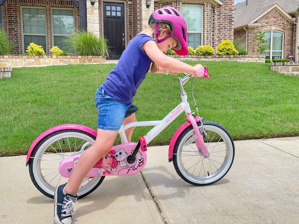 Child getting momentum on her by pushing off the ground as she's learning to ride her bike.