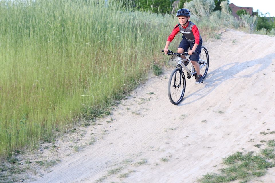 Boy riding Prevelo Alpha Four 24 inch bike down a sandy terrain hill