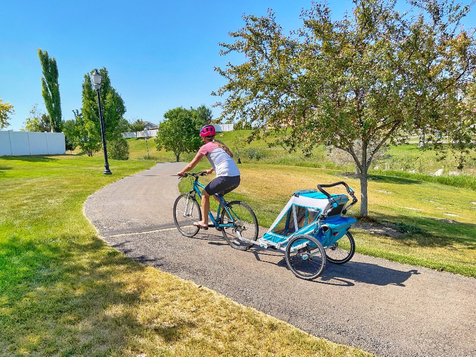 Mom pulling Qeridoo Speedkid trailer on paved trail