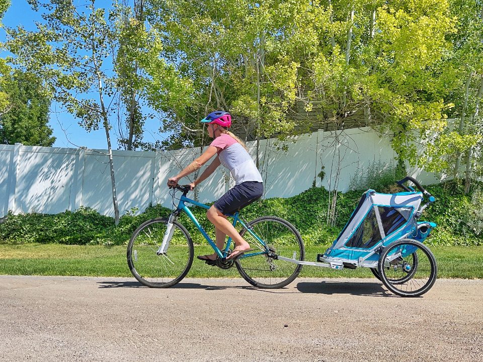 Mom pulling Qeridoo Speedkid trailer on paved trail through neighborhood