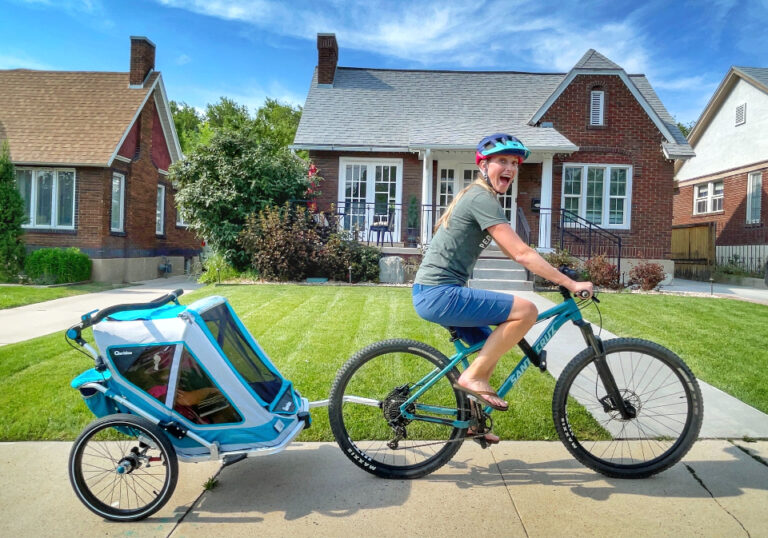Mom riding her bike down the sidewalk and pulling her toddler in the double capacity Speedkid bike trailer