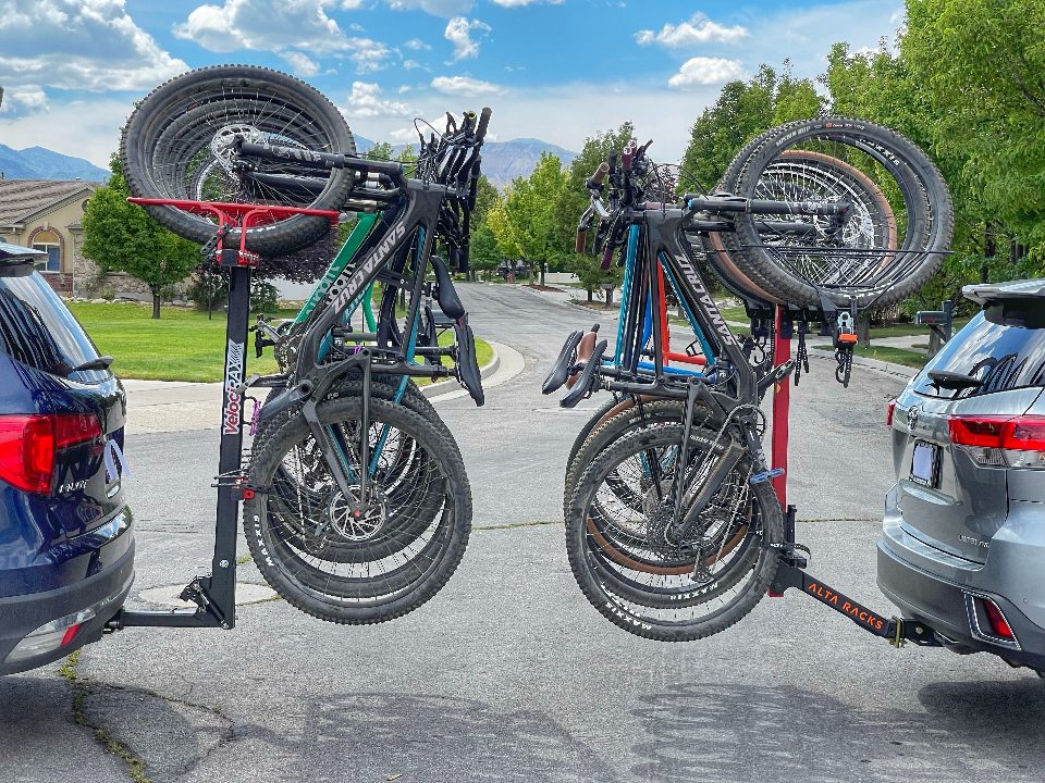 Two cars side by side with Velocirax and Alta Rack vertical bike racks fully loaded. Shown from side, with two cars backed up.
