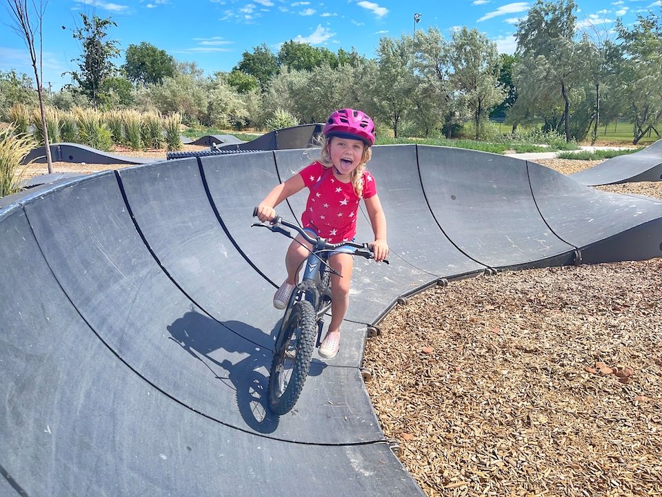 3 year old riding on black pump track on her Prevelo mountain bike