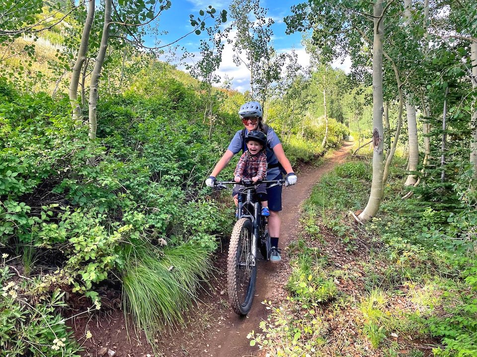 Mom riding through Alpine trees  with Shotgun Pro seat