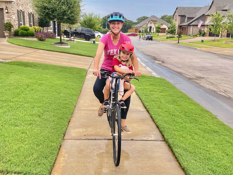 Front shot of Mom riding with toddler on her bike with the UrRider. Mom is bowing legs to ride.