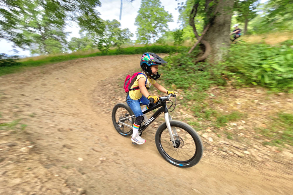 Young girl riding woom OFF 4, on a downhill section of trail