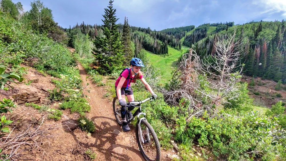young girl riding the woom oFF AIR 6 down a trail in park city, utah