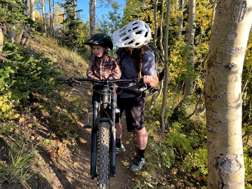 Mom standing next to her 2-year-old sitting on his Mac Ride seat on her mountain bike.