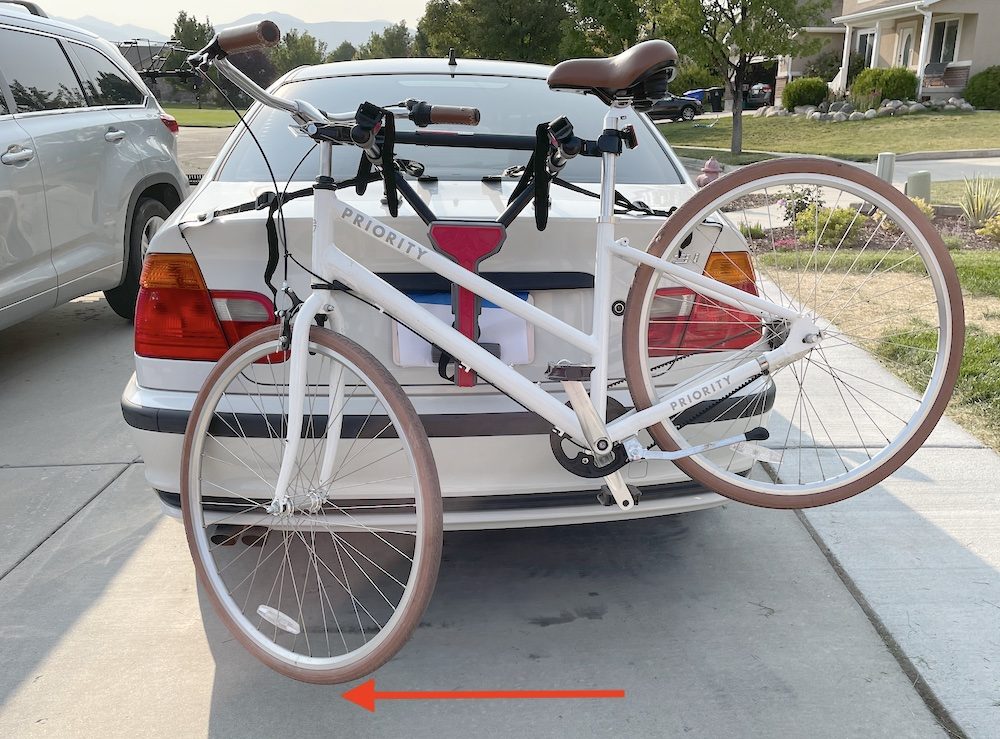 Adult bike with large wheels has front wheel very close to ground when loaded on a trunk rack with a top tube adapter bar.