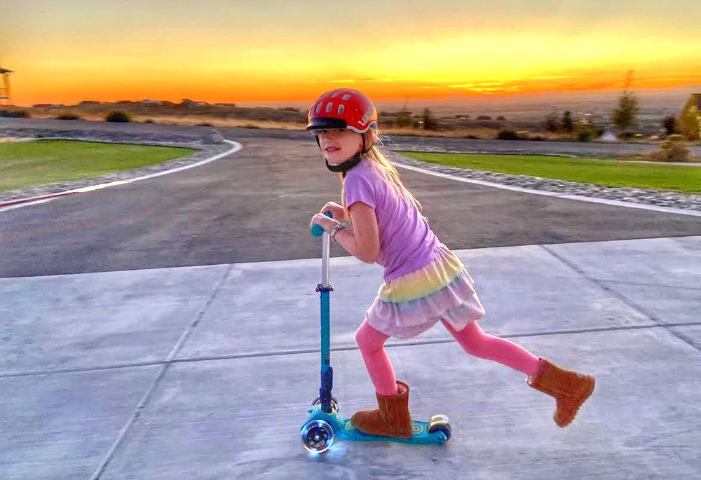 Girl riding Micro scooter with LED light up wheels at dusk