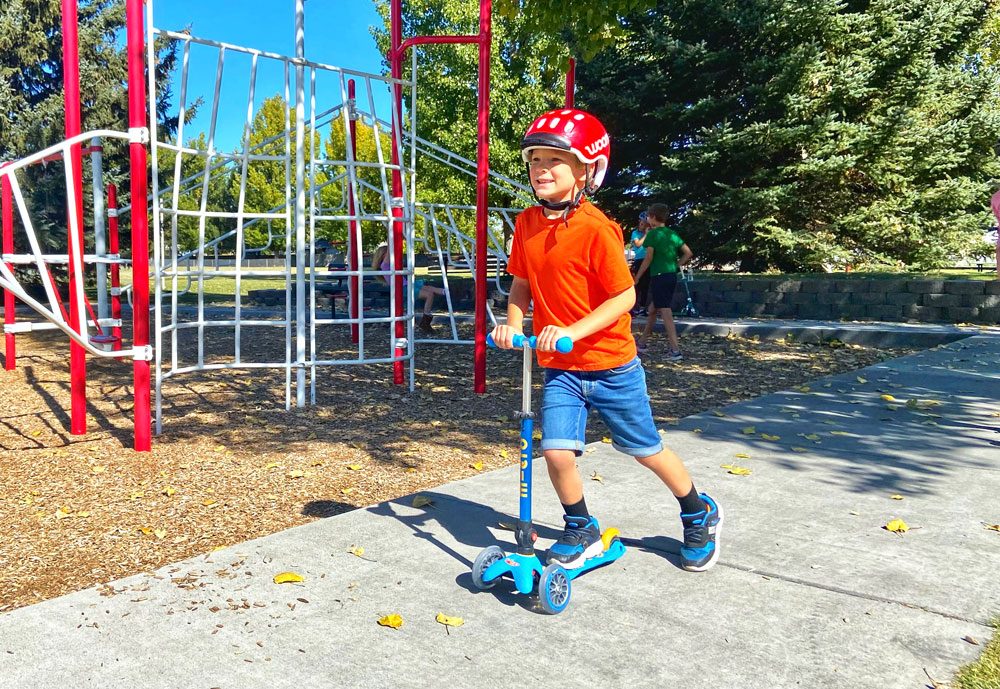 Boy riding Micro Mini scooter through the park