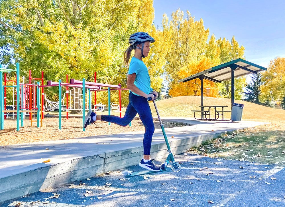 Girl leaping off the curb riding the Micro Sprite kids scooter