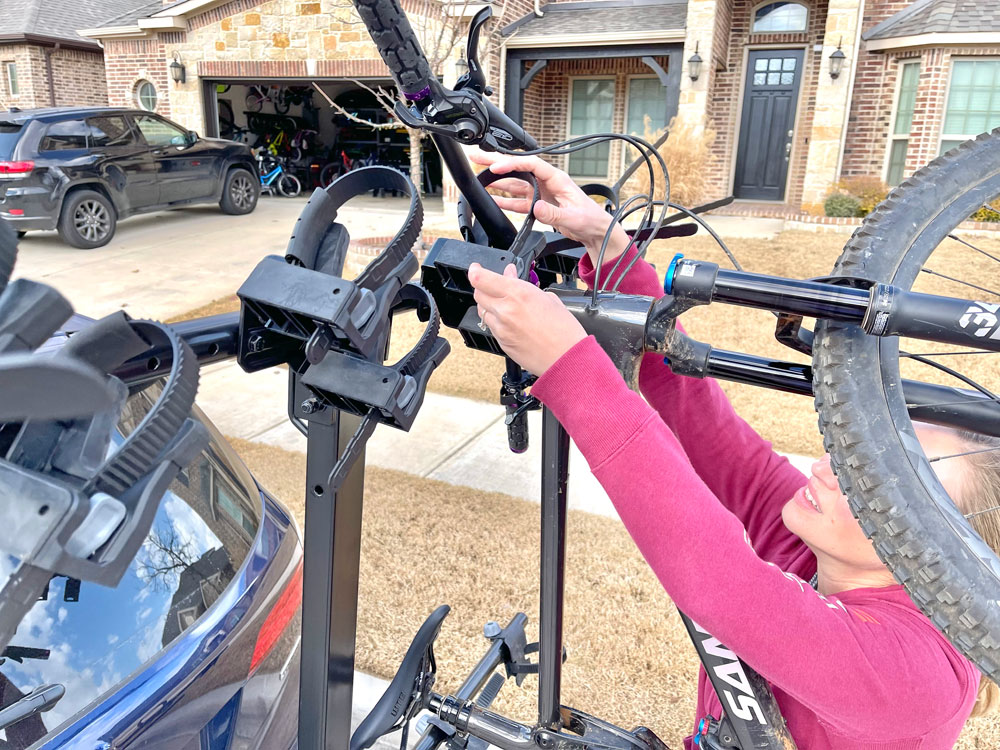 Woman reaching high to secure the handlebar straps on the Yakima HangTight bike rack