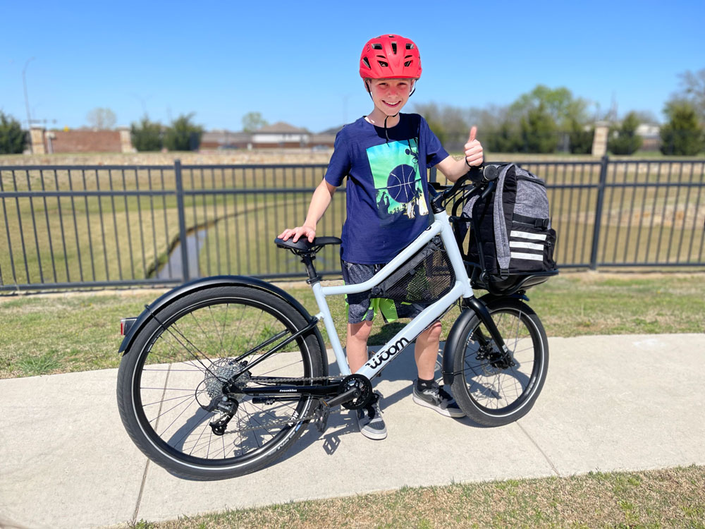 11 year old boy standing with his woom NOW 6 26 inch kids commuter bike on a paved path