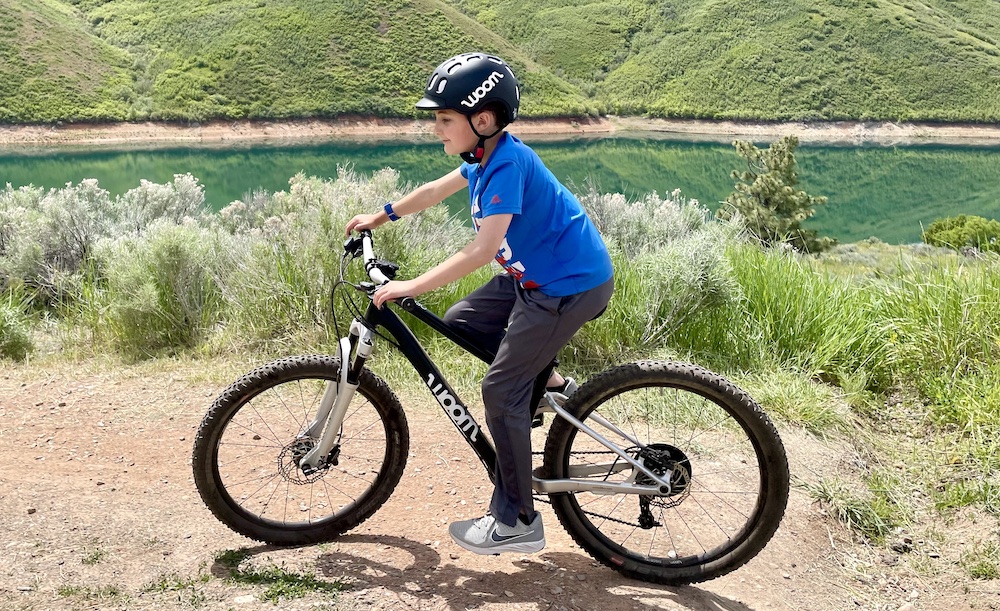 Boy riding woom bike while wearing woom kids helmet in black