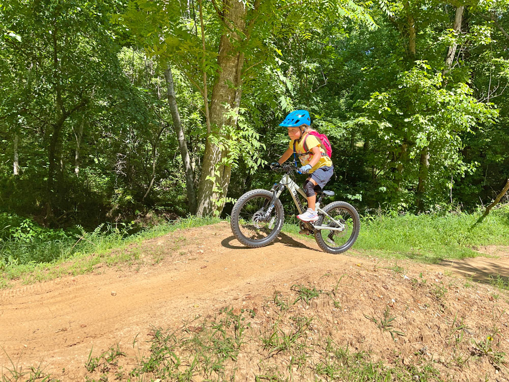 Child standing and climbing up small roller on Prevelo 20" mountain bike on All-American trail in Bentonville