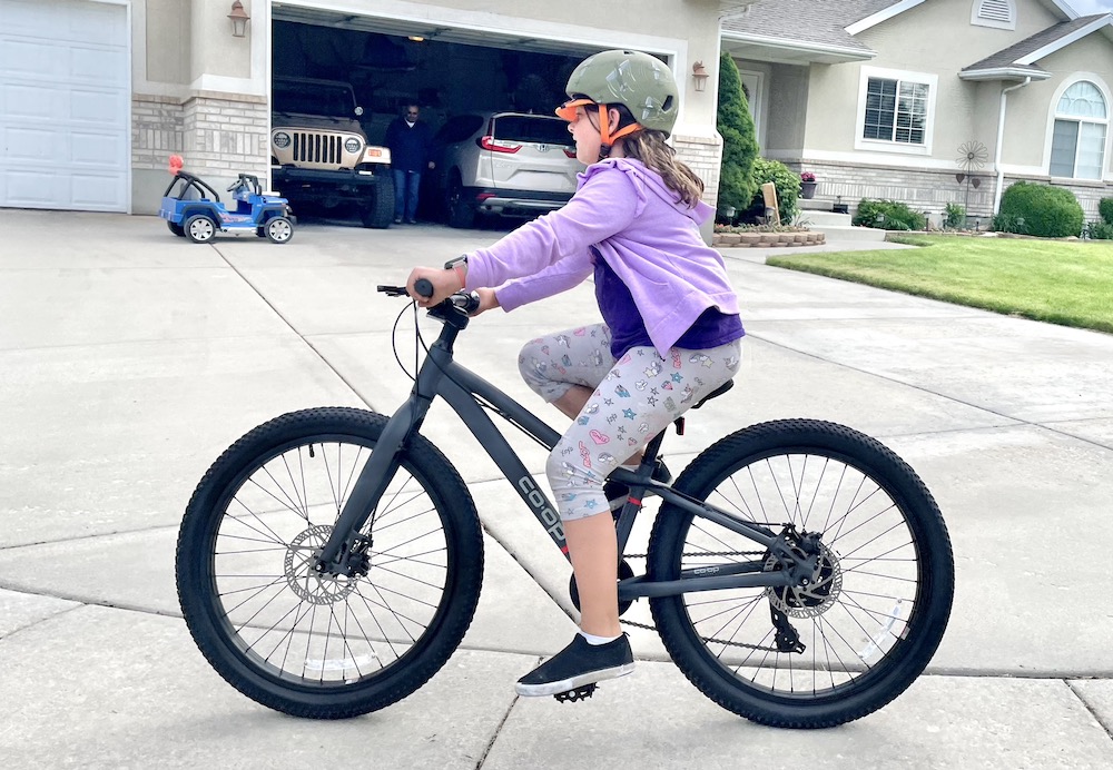 girl riding the REI REV 24 inch kids bike on a sidewalk