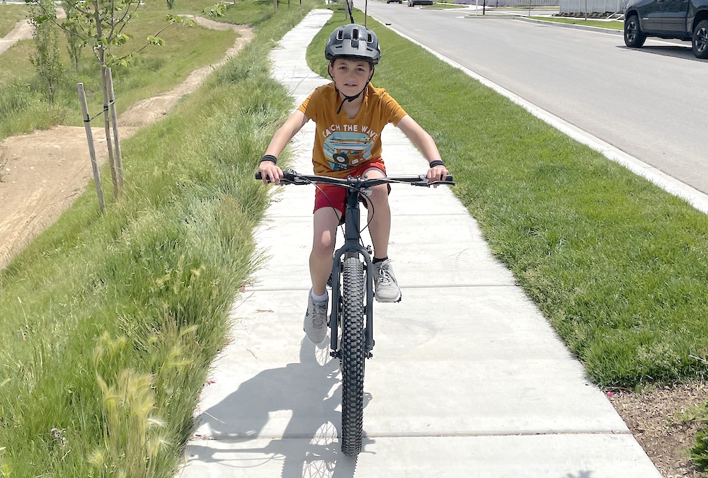 young rider riding the REI REV 24" mountain bike coming towards the camera showing how wide the handlebars are