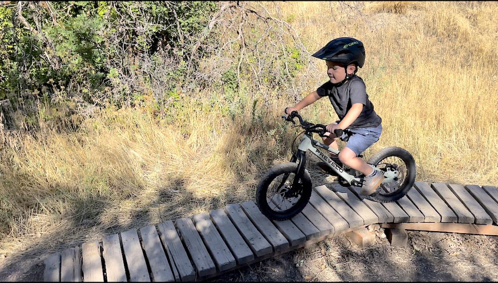3 year old boy riding Prevelo Zulu One kids mountain bike over a wood bridge feature
