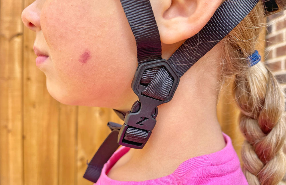 Buckle of Lazer Nutz kid helmet sits on the side of a child's neck