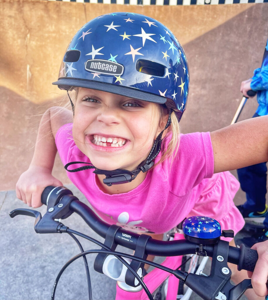 Girl wearing star pattern Little Nutty helmet with matching bell on her bike